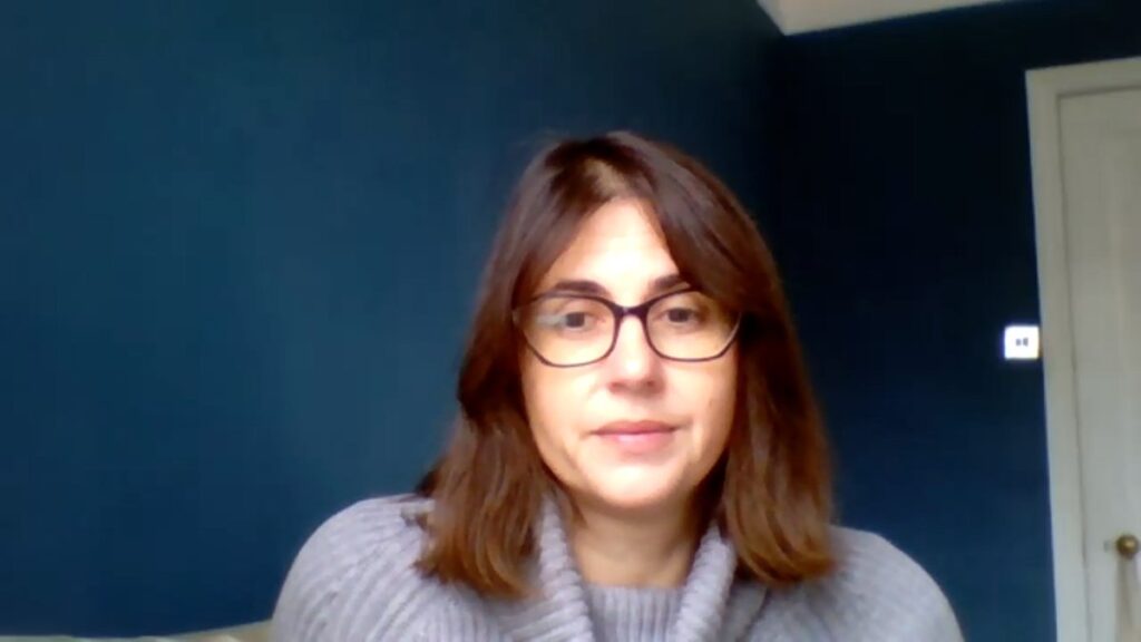 Foto dell’autrice con occhiali e maglione grigio davanti a una parete blu scuro